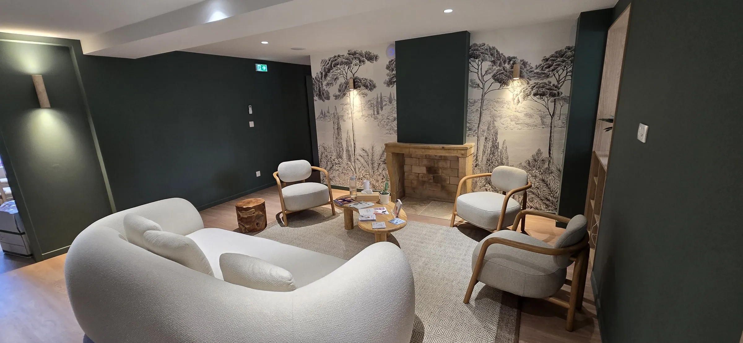 Salon d'attente : canapé blanc, fauteuils, papier peint forêt et murs vert sombre